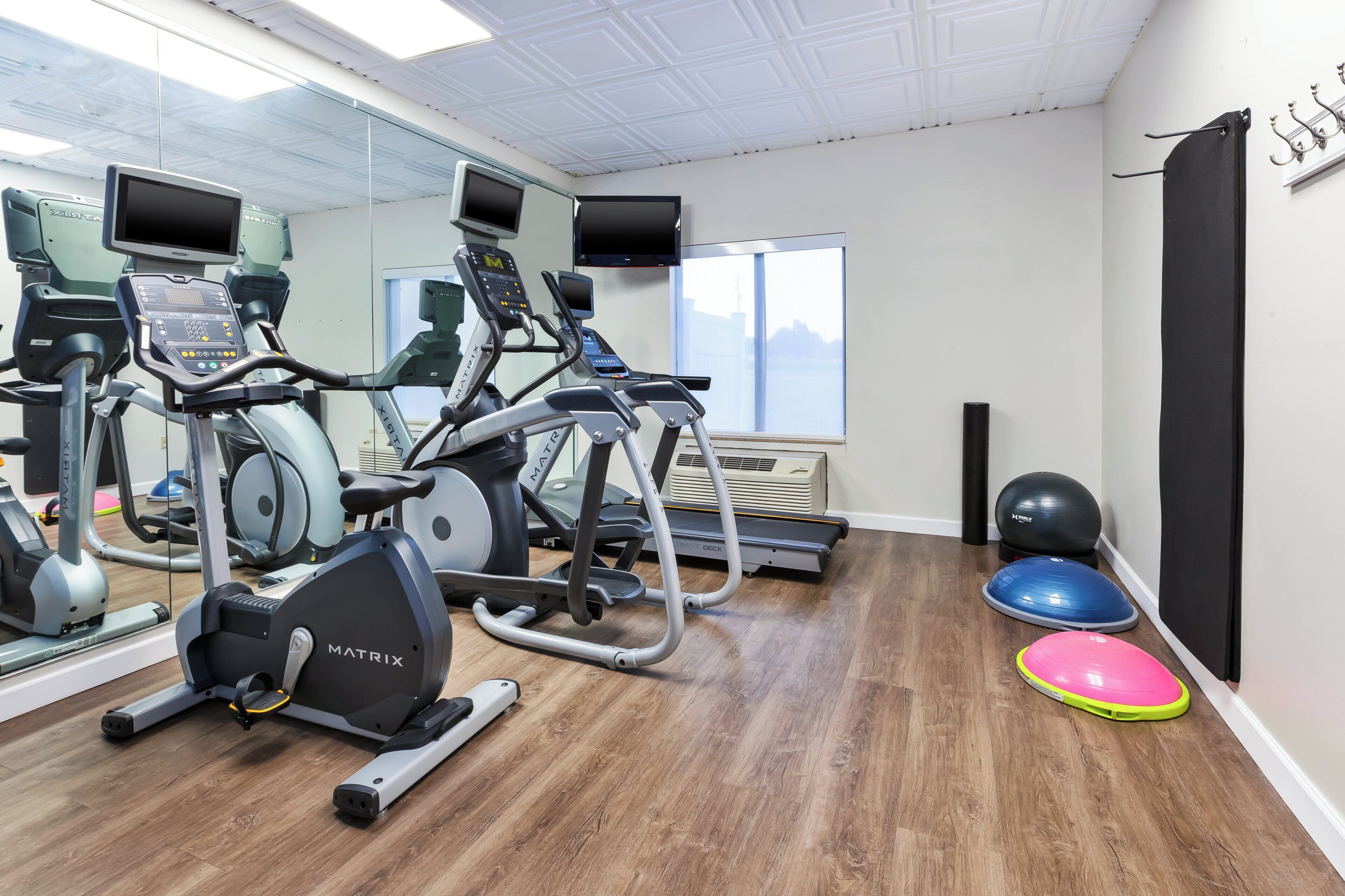 Un gimnasio con máquinas de cardio, un espejo grande y un amplio ventanal.