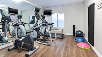 Un gimnasio con máquinas de cardio, un espejo grande y un amplio ventanal.