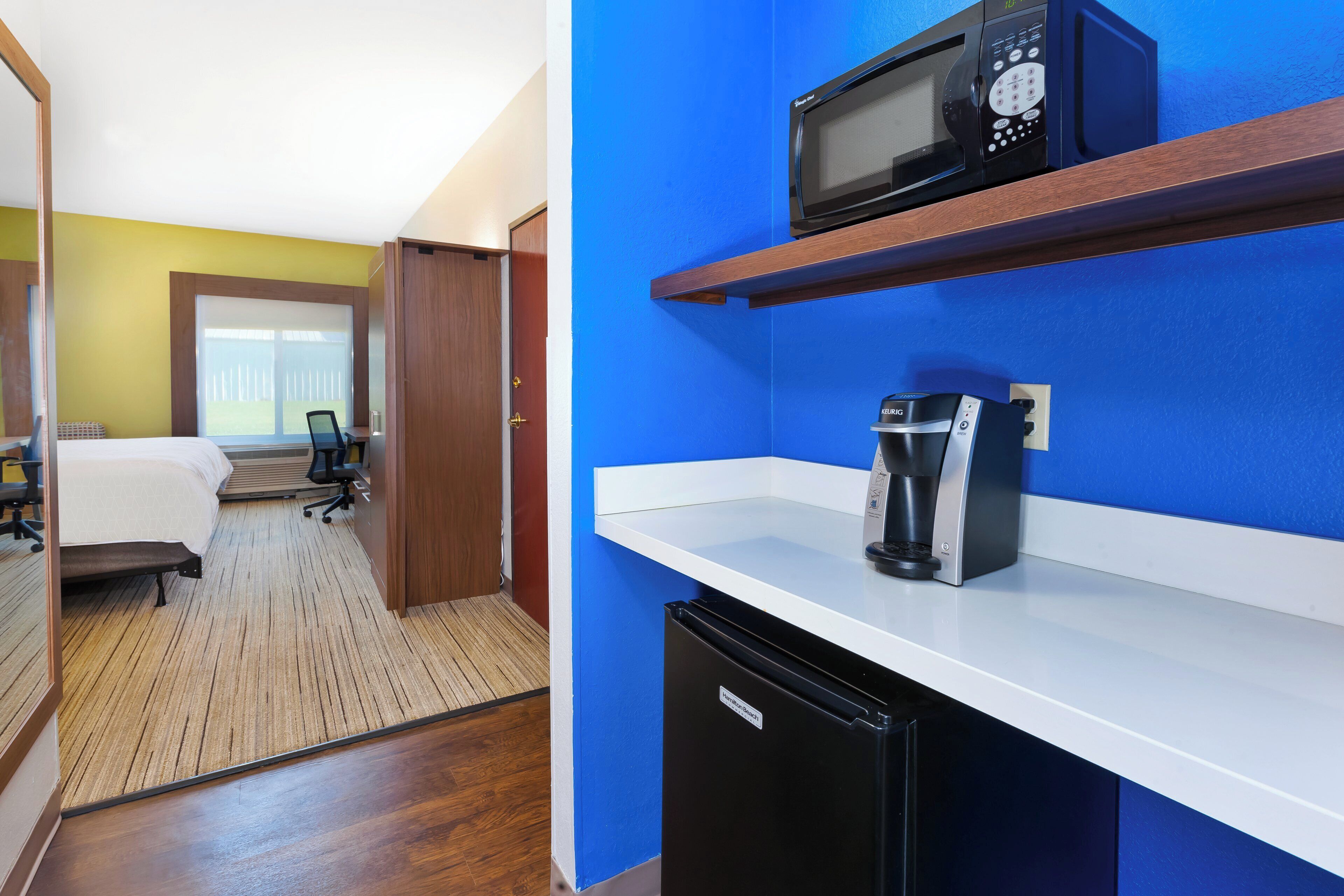 Habitación de hotel con cama, escritorio, silla y kitchenette.
