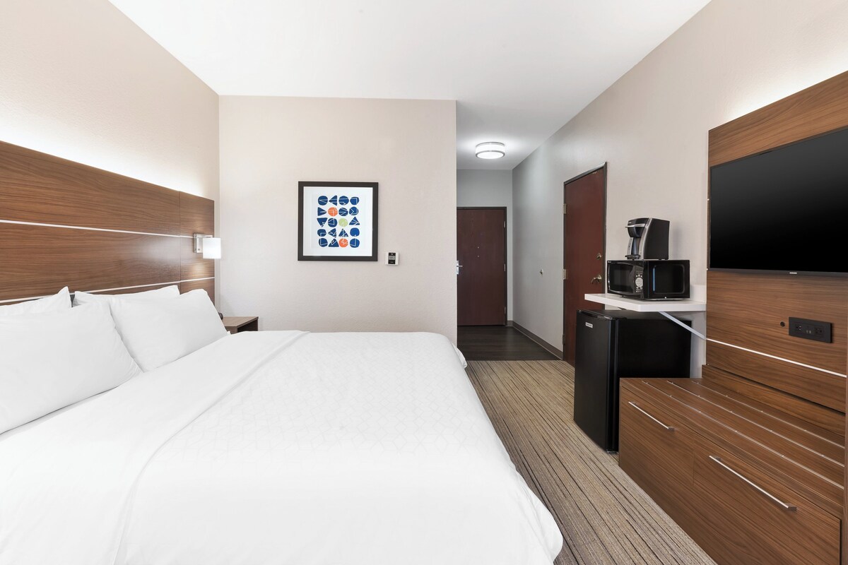 Habitación de hotel con una cama grande, un televisor, una cafetera y un cuadro en la pared.