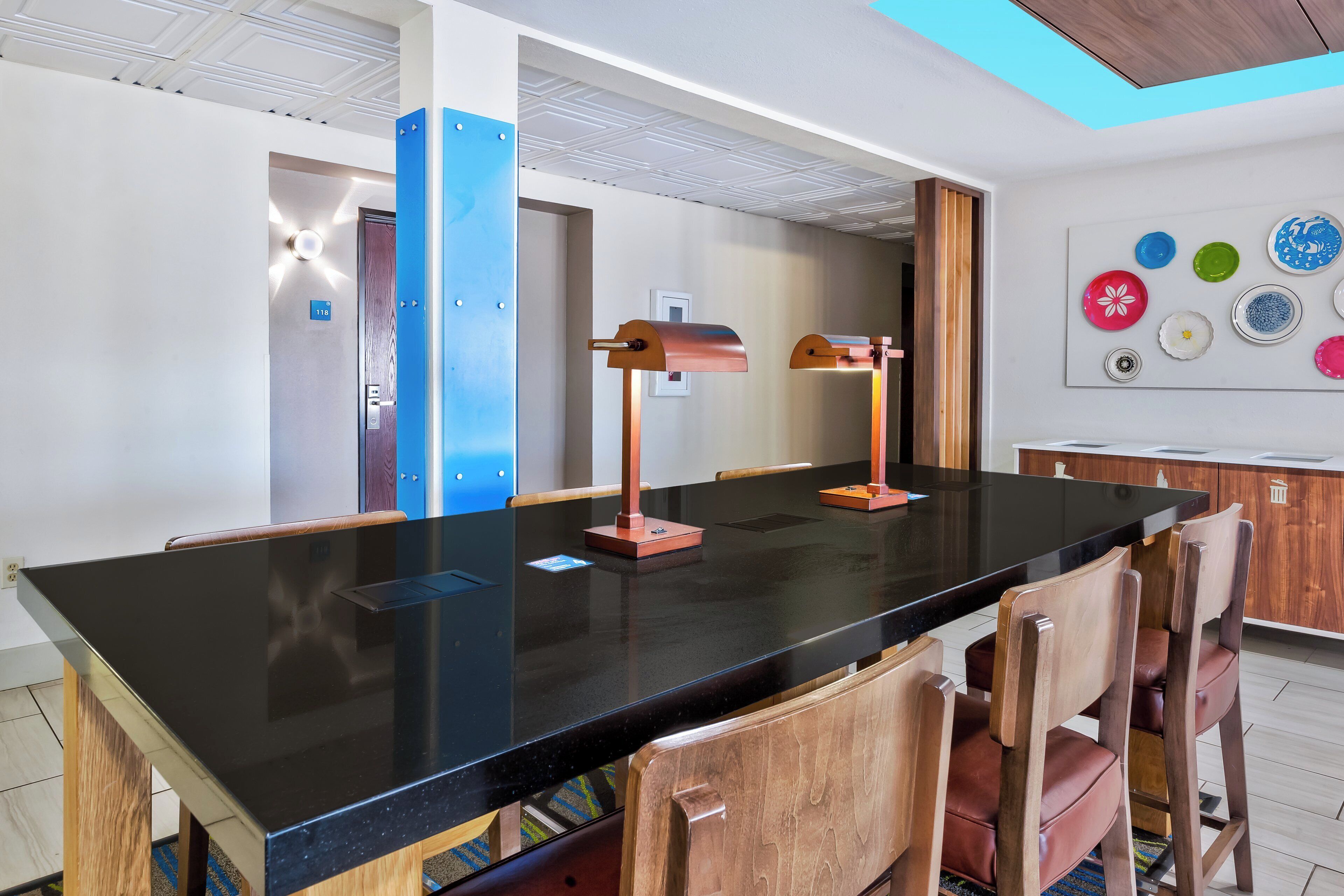A conference room with a black table, wooden chairs, and two standing lamps.