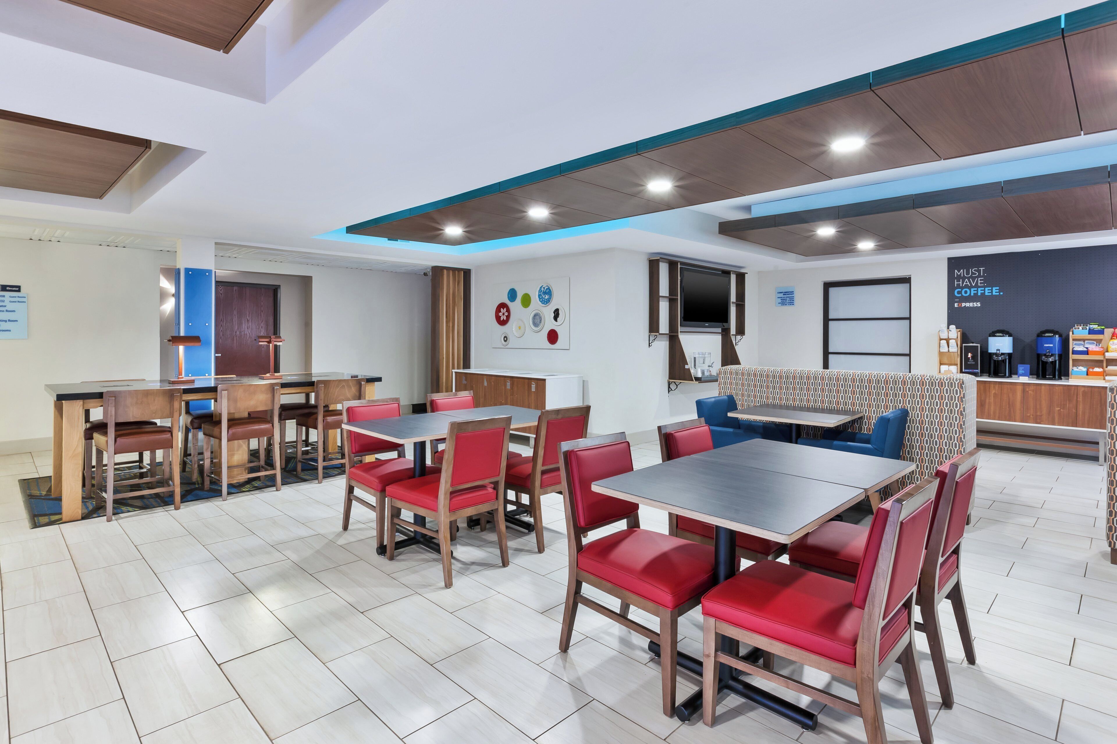 A modern dining area with wooden tables and red chairs, a flat-screen TV, and a coffee station.