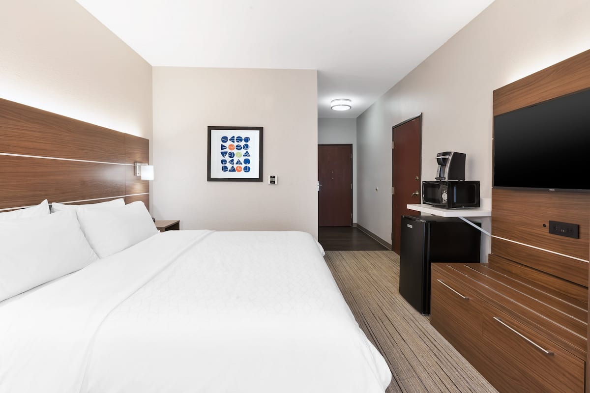 A hotel room with a large bed, a flat-screen TV, a coffee machine, and a wooden dresser.