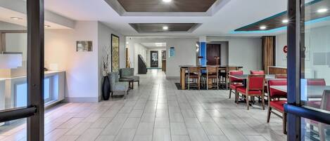 A hotel lobby with a modern design, featuring a check-in desk, seating area, and a staircase leading to other floors.