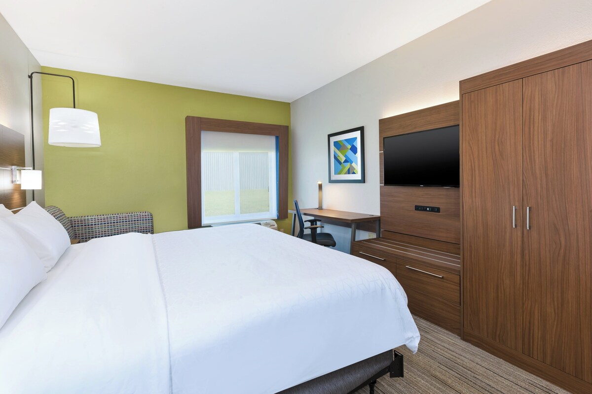 Habitación de hotel con cama, escritorio, televisor, armario y ventana con persianas.