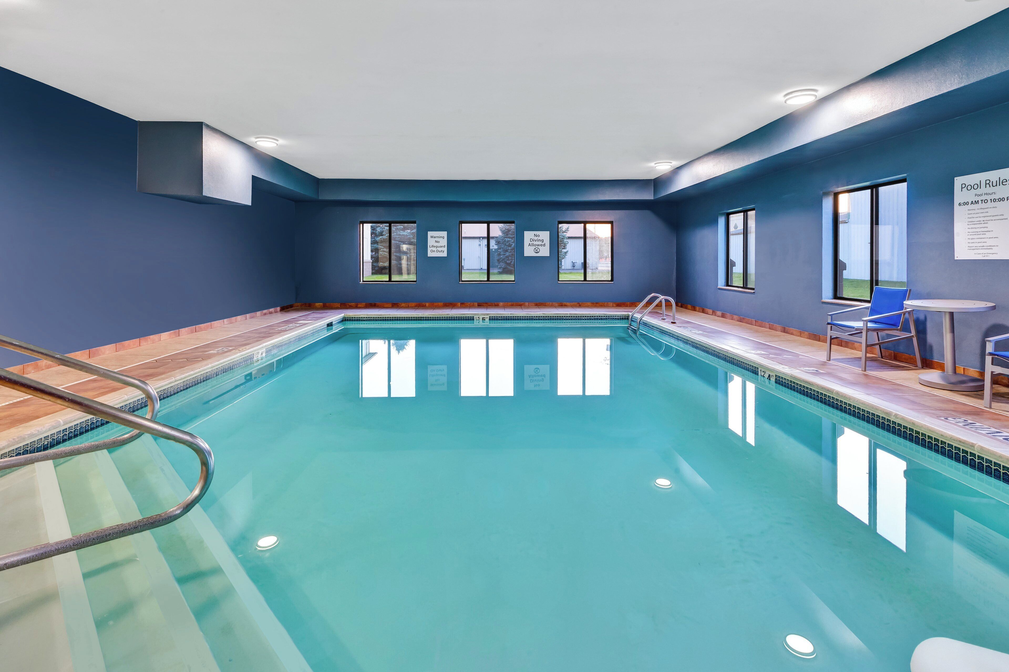 An indoor swimming pool with clear water, a diving board, and a lifeguard chair.