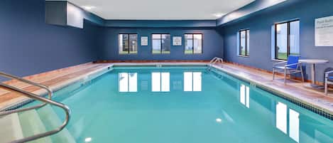 An indoor swimming pool with clear water, a diving board, and a lifeguard chair.