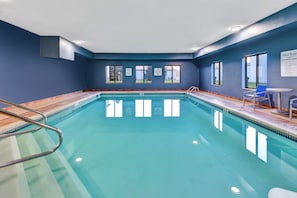 An indoor swimming pool with clear water, a diving board, and a lifeguard chair.
