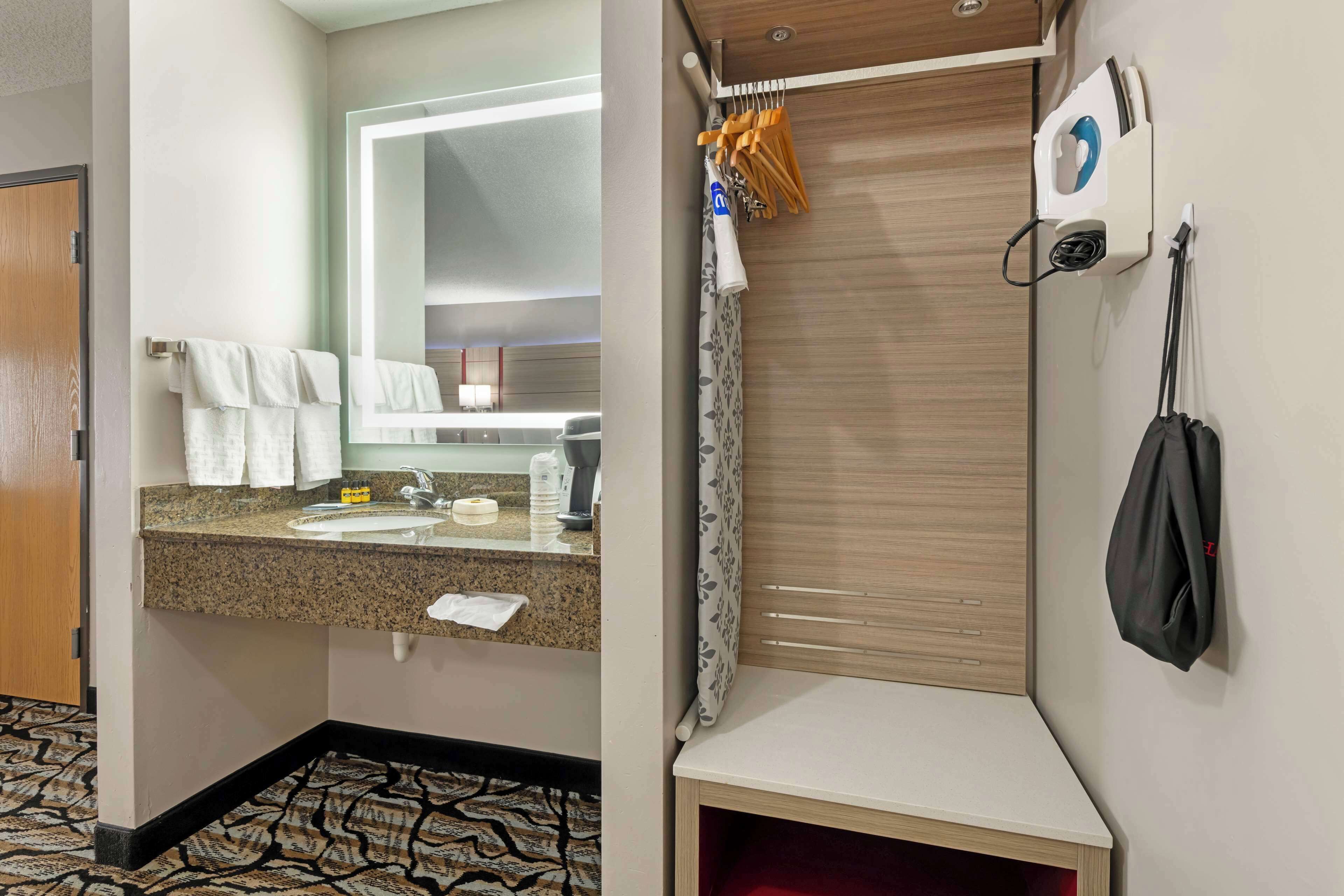 A hotel bathroom with a sink, mirror, towel rack, shower curtain, and a towel hanging on the wall.