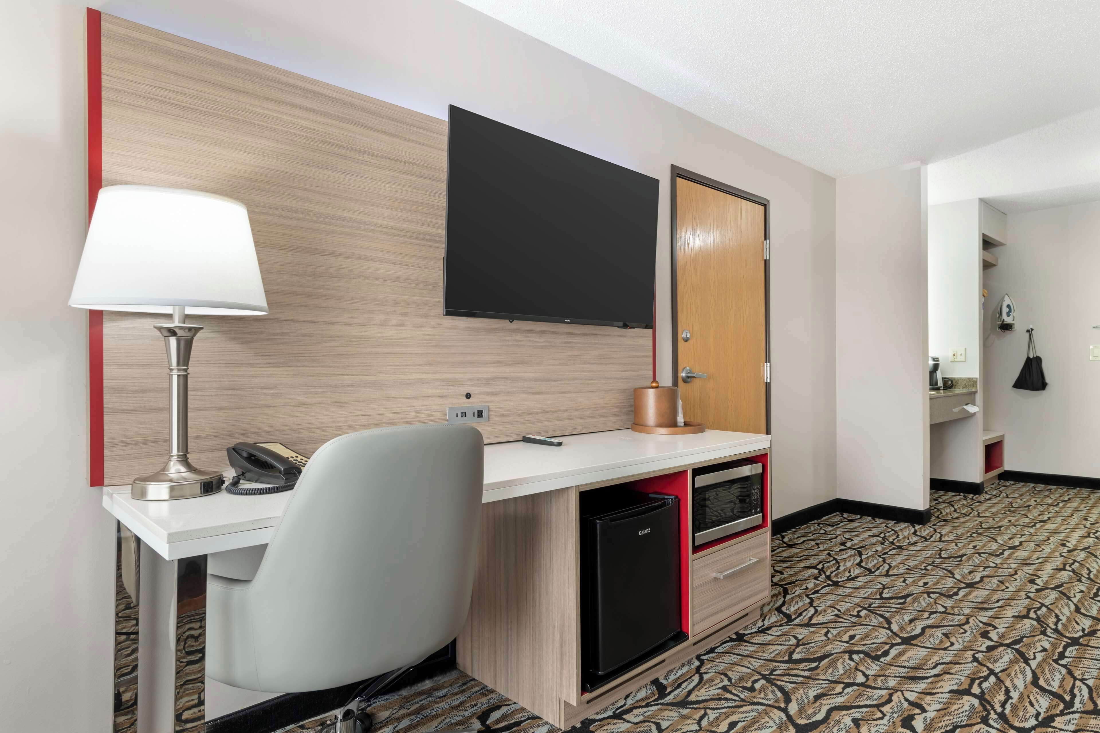 Een hotelkamer met een bureau, stoel, flatscreen-tv, minibar en een kamerbreed tapijt.