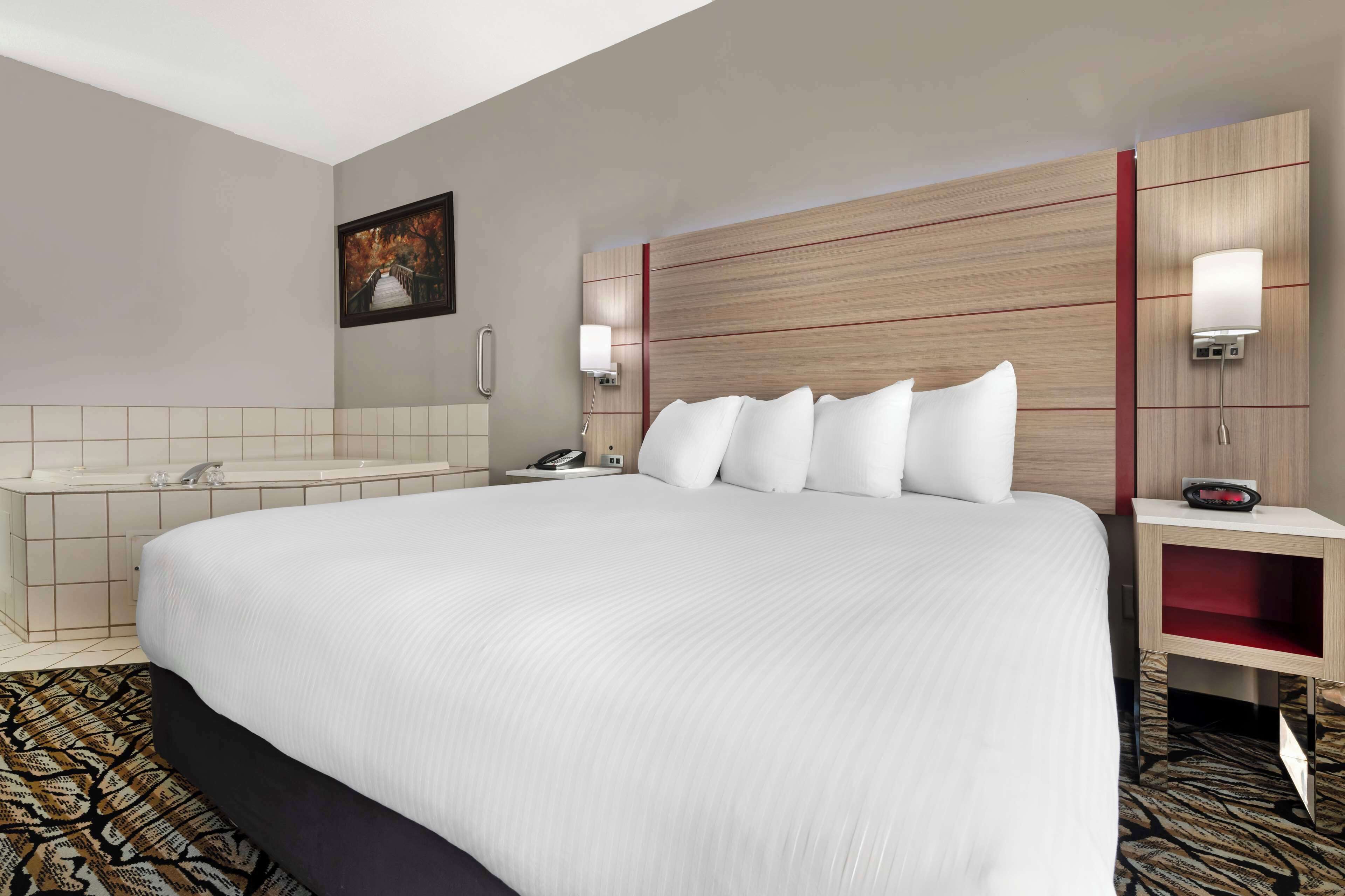 Habitación de hotel con una cama grande, un baño con bañera y un escritorio pequeño con teléfono.