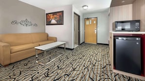 Una habitación de hotel con alfombra estampada, un sofá, una mesita, un microondas y un refrigerador.