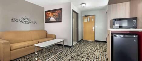 A hotel room with a patterned carpet, a sofa, a small table, a microwave, and a refrigerator.
