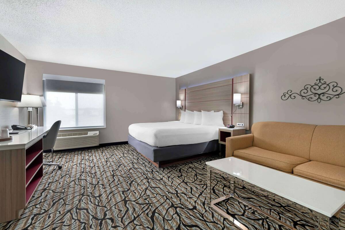 Ein Hotelzimmer mit Bett, einer Couch, einem Schreibtisch, einem Fernseher und einem Fenster.