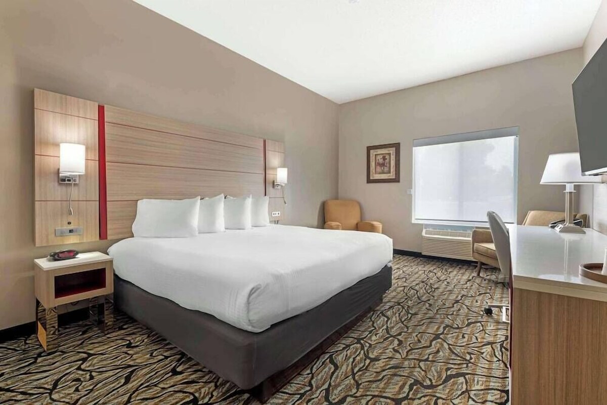 A hotel room with a large bed, a desk with a chair, a window, and a wall-mounted TV.
