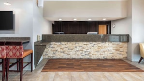 Un área de recepción con pared de piedra, un televisor de pantalla plana, un reloj y una zona de estar con sillones estampados.