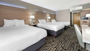 Una habitación de hotel con tres camas, un escritorio y una alfombra estampada.