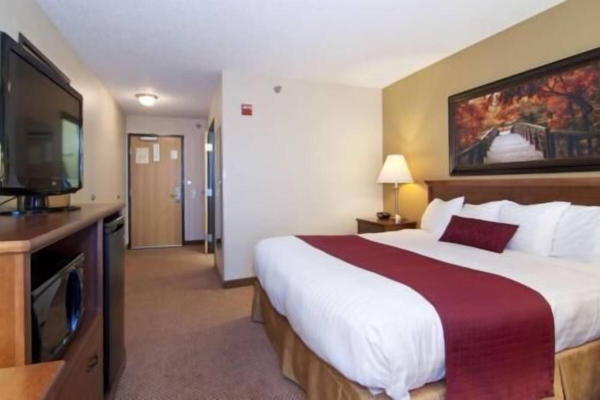 Ein Hotelzimmer mit einem Bett, einem Fernseher, einem Gemälde und einer Tür zu einem weiteren Zimmer.