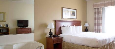Une chambre d’hôtel avec un grand lit, une table de chevet avec des lampes, un téléviseur posé sur une commode et une baignoire avec des serviettes.