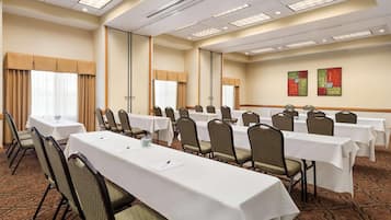 A conference room with multiple tables and chairs, large windows with curtains, and artwork on the walls.
