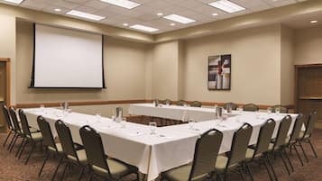 A conference room with long tables, chairs, a projector screen, and a painting on the wall.