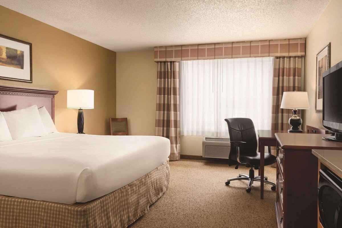 A hotel room with a large bed, a desk with a chair, a television, and a window with curtains.