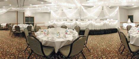 A banquet hall with round tables set for dining, covered with white tablecloths and arranged in rows.