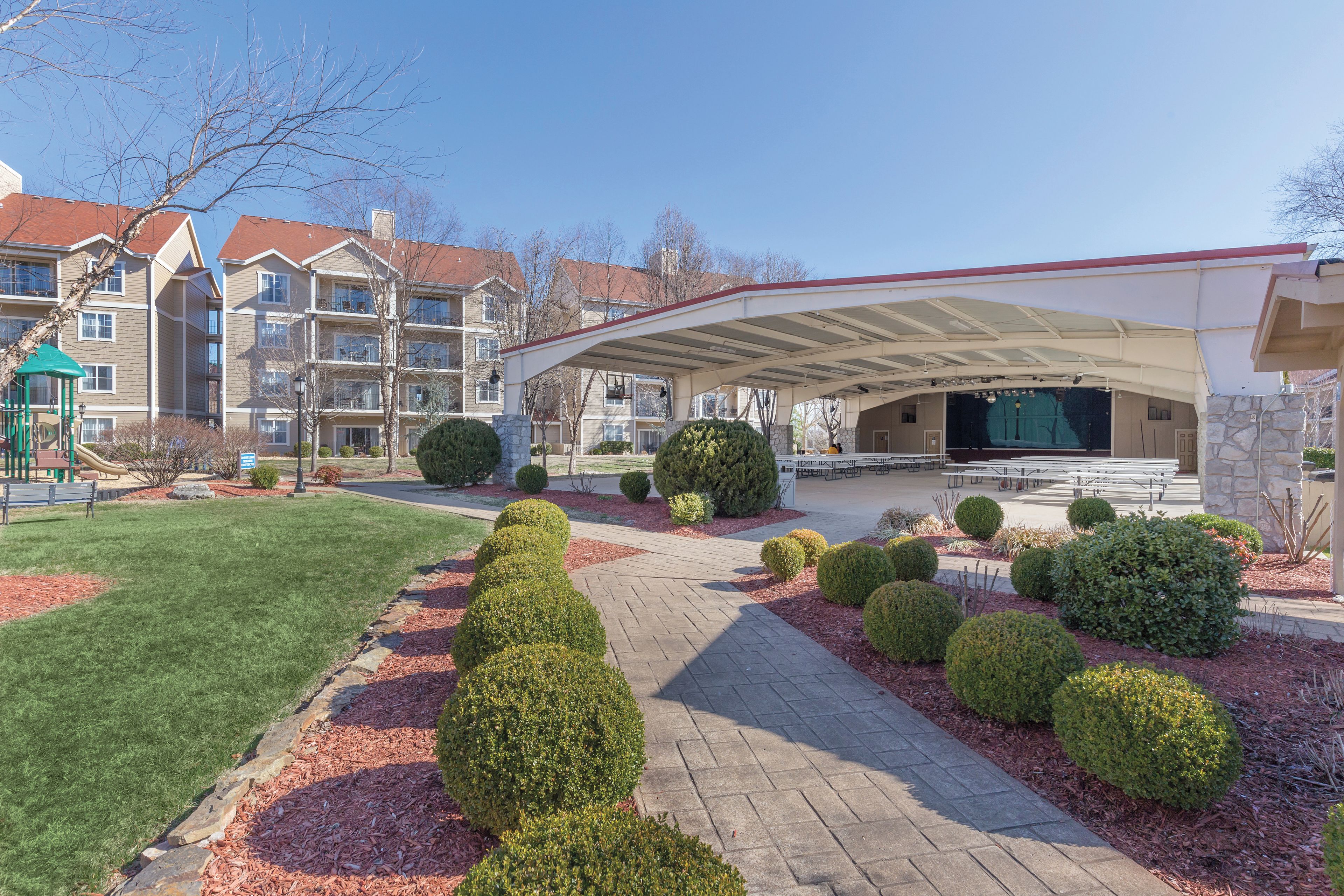 A courtyard with a covered seating area, a playground, and a pathway lined with shrubs.