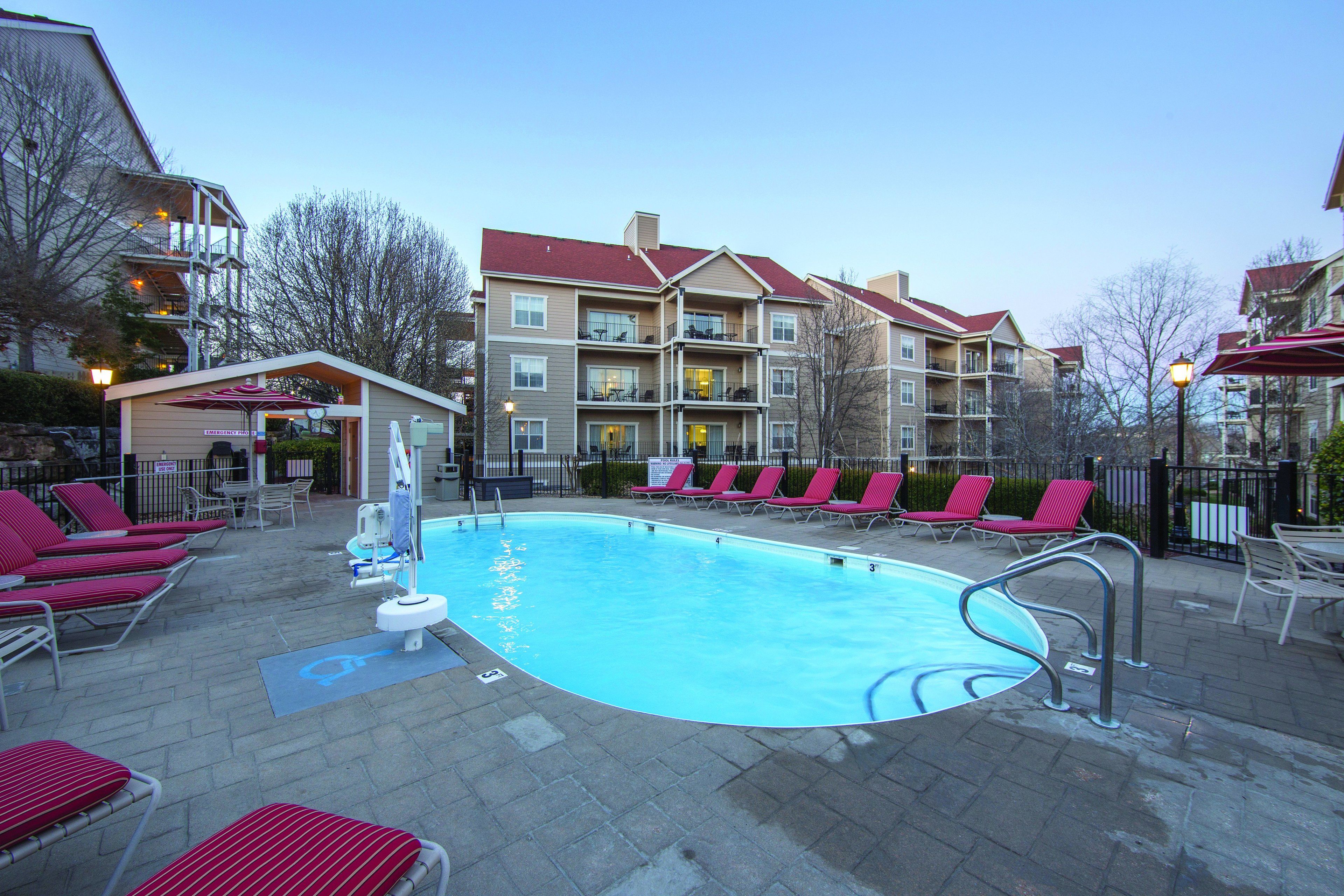 A swimming pool with red lounge chairs and a wheelchair-accessible area.