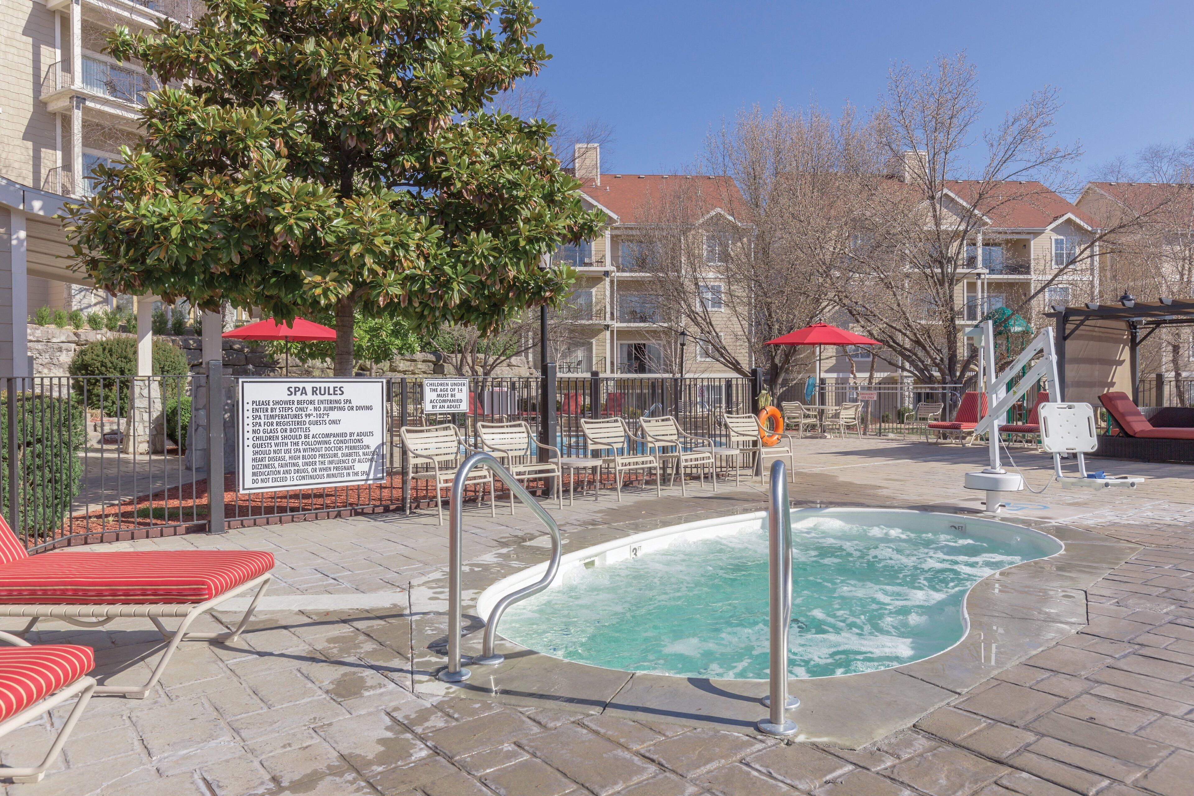 A pool area with lounge chairs, a hot tub, and a sign detailing spa rules.