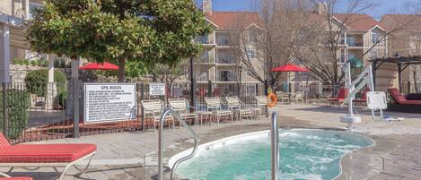 A pool area with lounge chairs, a hot tub, and a sign detailing spa rules.