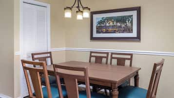 A dining room with a wooden table and chairs, a chandelier, a framed picture on the wall, and a white door.