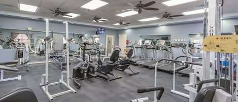 Un gimnasio con varios equipos de ejercicio, ventiladores de techo y un letrero para la banca vertical SOHN.