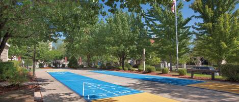 A park with a shuffleboard court, trees, and a flagpole.