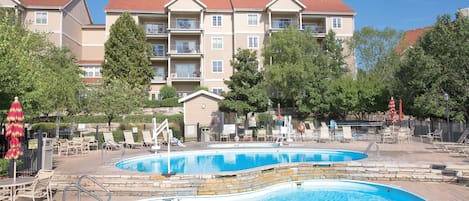 A pool area with two pools, lounge chairs, and a building with balconies in the background.