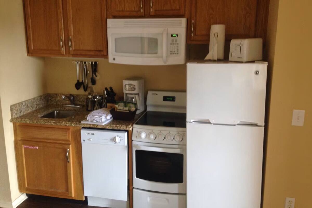 Una cocina con gabinetes de madera, microondas, estufa y refrigerador.