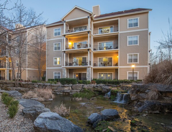 A multi-story hotel with balconies, a small waterfall feature, and a stone retaining wall.