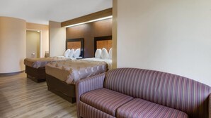 Habitación de hotel con dos camas, un sofá y un espejo grande.