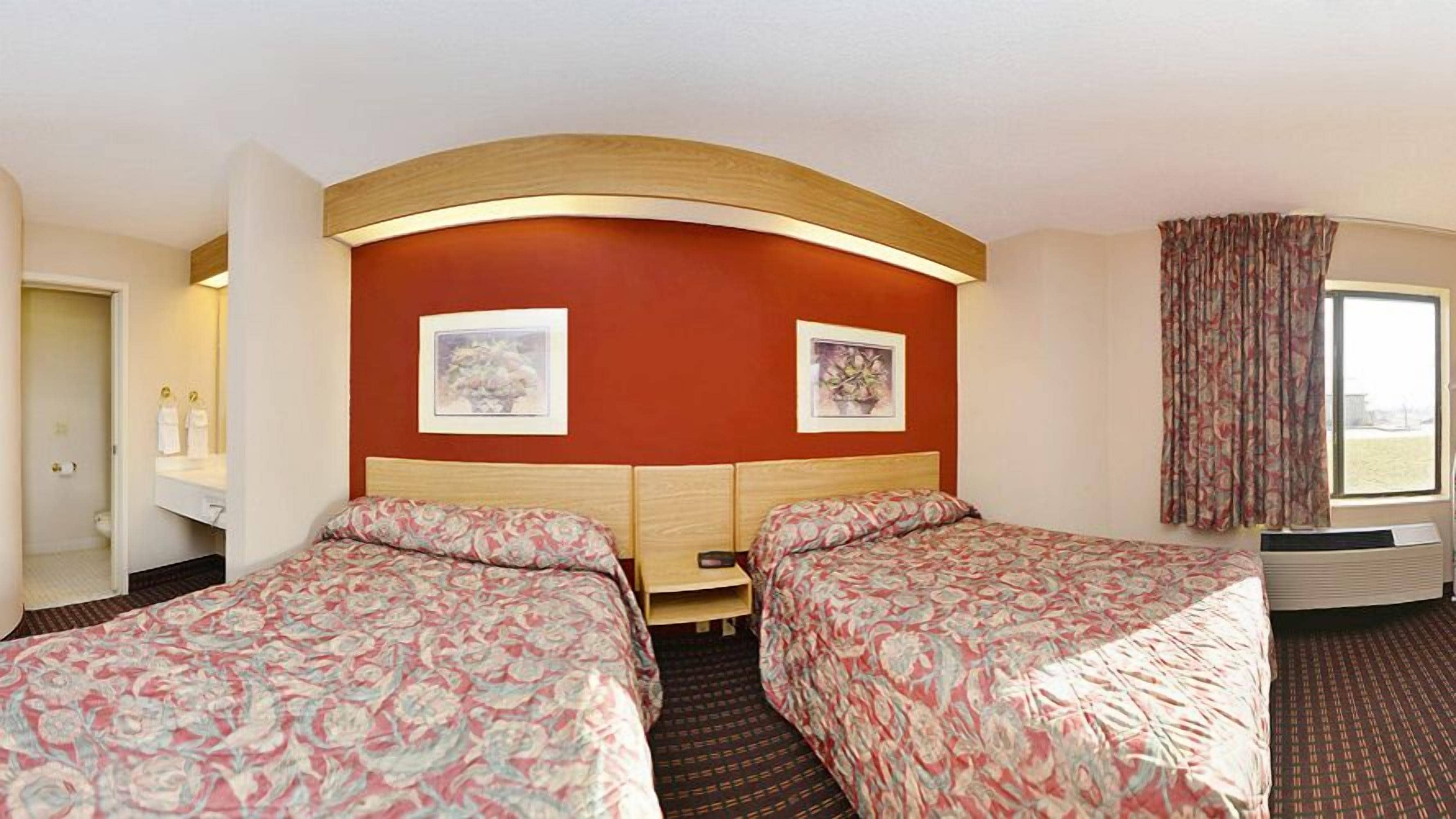 A hotel room with two beds, a large window with curtains, a mirror, and two framed pictures on the wall.