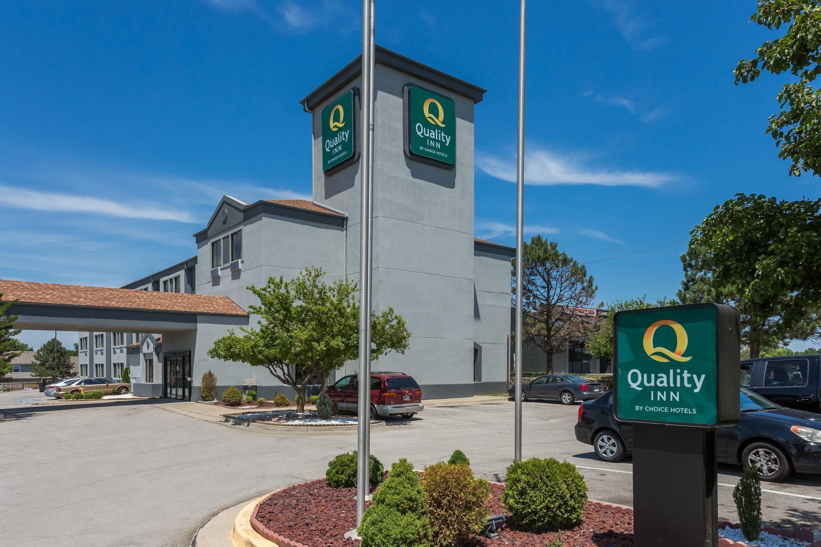 Ein Quality Inn by Choice Hotels mit einem markanten Turm, einem Parkplatz und blauem Himmel.