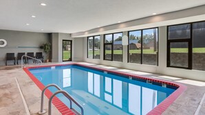 Una piscina rectangular interior con un borde de azulejos rojos y azules, rodeada de suelo de piedra y ventanas grandes.