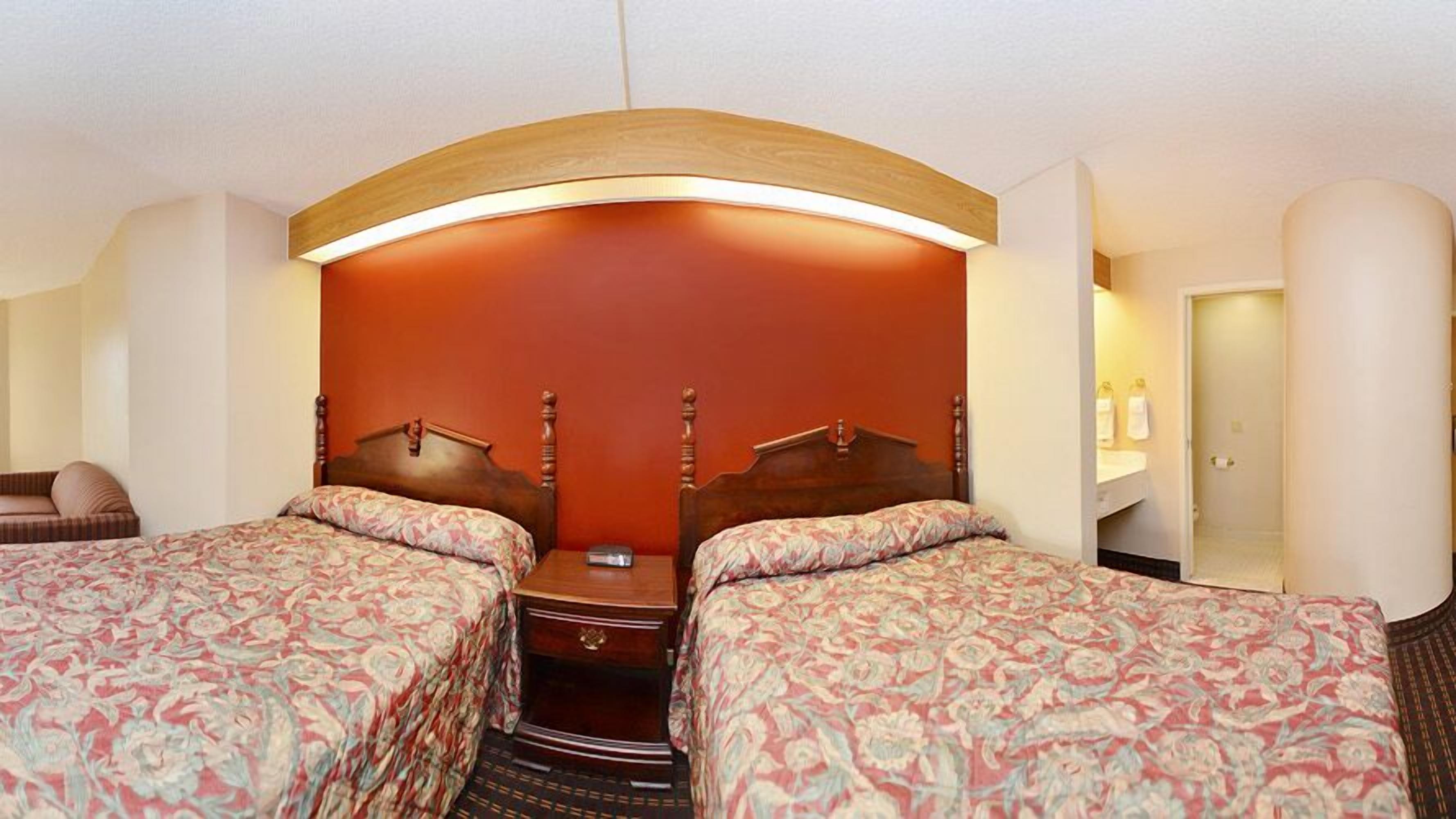 A hotel room with two beds, a wooden headboard, a bedside table, and a bathroom visible through an open door.