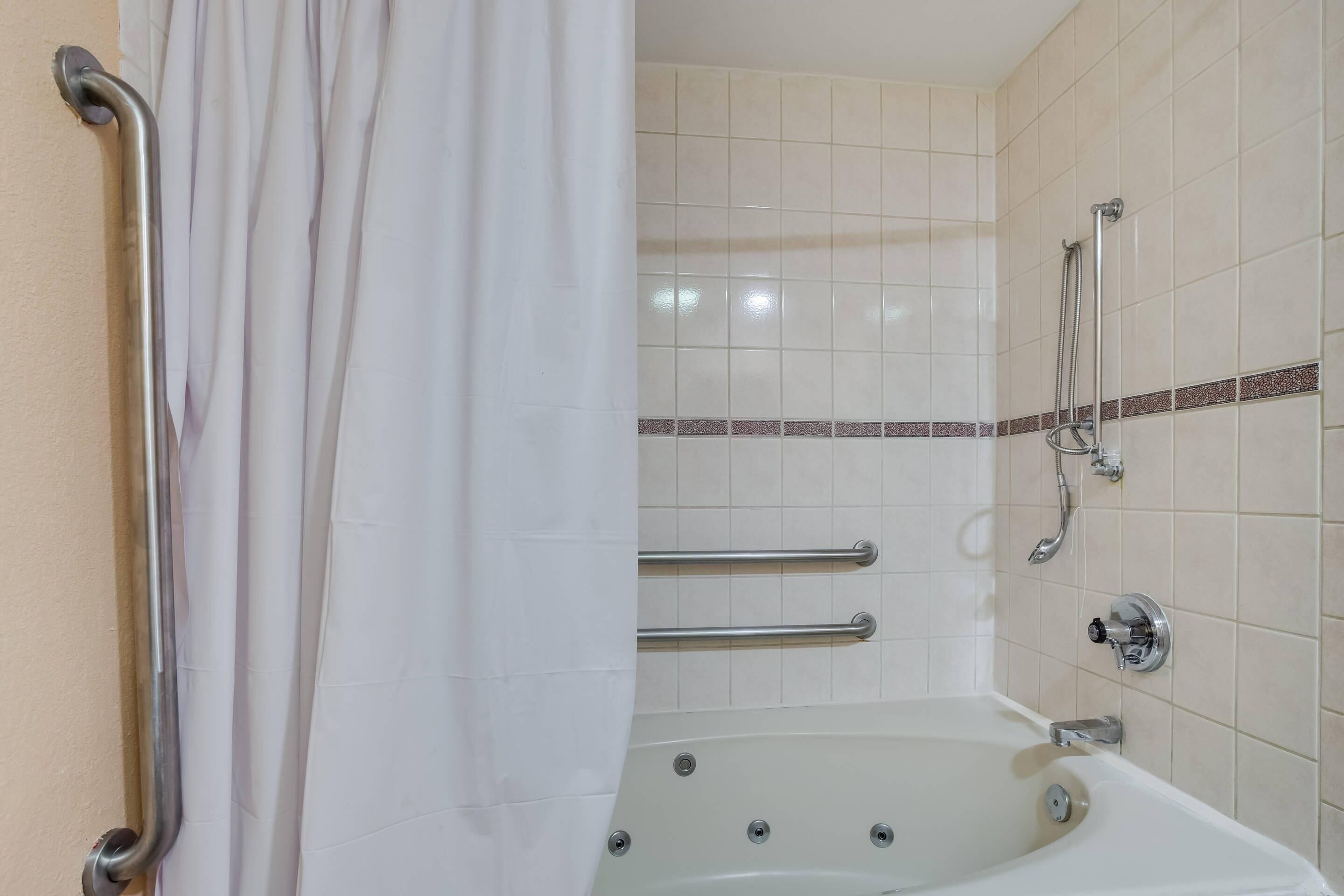 A bathroom with a bathtub, grab bars, and a shower area.