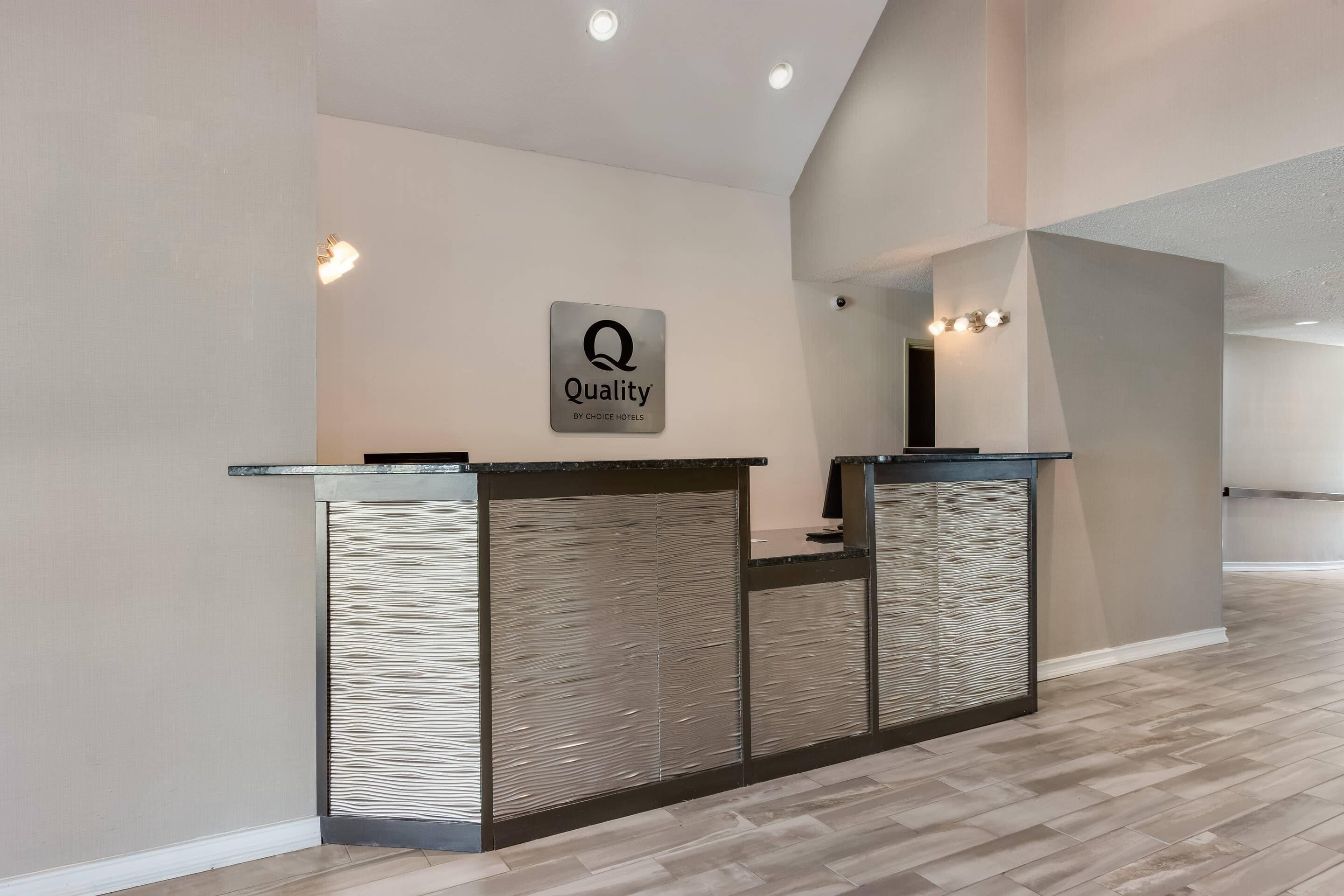 A reception desk with a 'Quality by Choice Hotels' sign, a modern design with a textured panel, and a clean, minimalist interior.