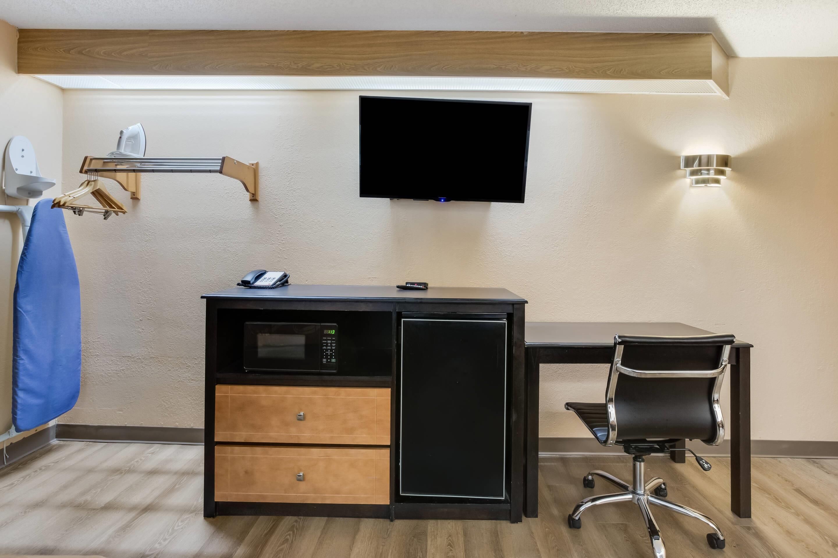 Habitació d'hotel petita amb escriptori, televisió penjada a la paret, microones i frigorífic petit.