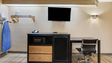 A compact hotel room with a desk, a TV mounted on the wall, a microwave, and a small refrigerator.