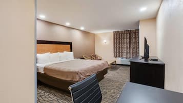 A hotel room with a bed, a desk, a chair, a television, and a patterned carpet.