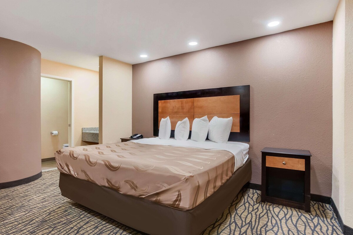 A hotel room with a large bed, a bedside table, and a nightstand.
