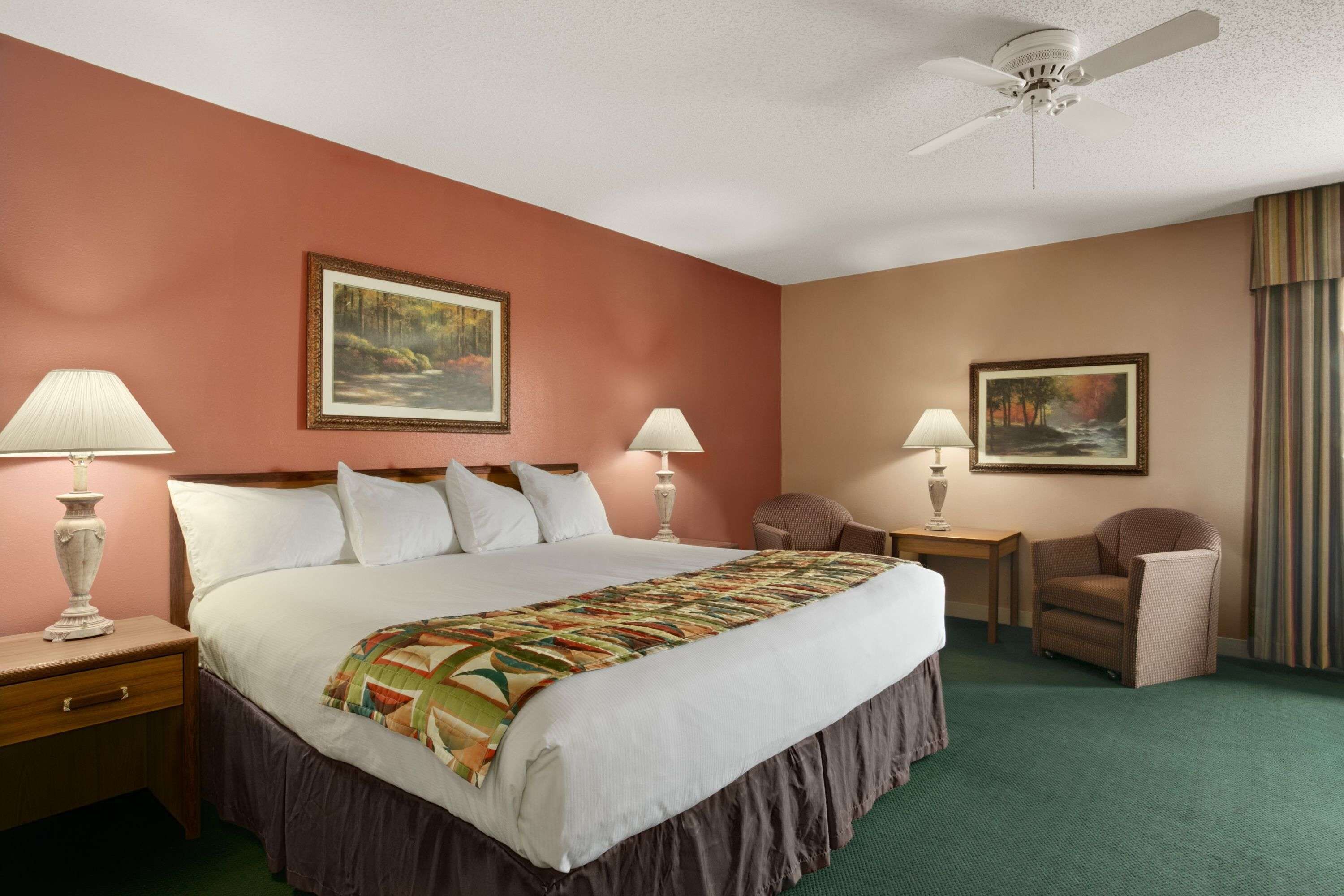 A hotel room with a large bed, two bedside tables with lamps, a chair, and a ceiling fan.