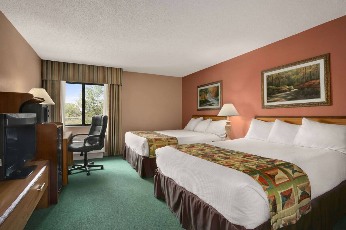 A hotel room with two beds, a desk with a television, and a chair.